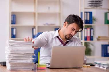 Genç bir erkek çalışan ve ofiste çok fazla iş var.