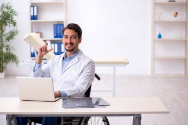 Klinikte çalışan tekerlekli sandalyedeki genç erkek doktor.