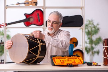 Yaşlı erkek tamirci iş yerinde müzik aletlerini tamir ediyor.