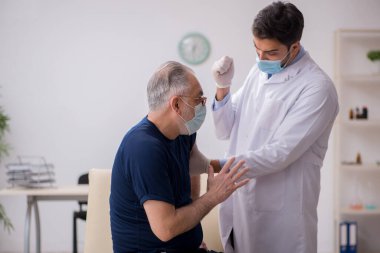 Yaşlı bir erkek hasta aşıyla genç bir doktoru ziyaret ediyor.