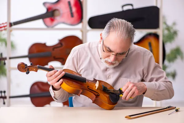 Viejo reparador masculino reparando instrumentos musicales en el lugar de trabajo — Foto de Stock