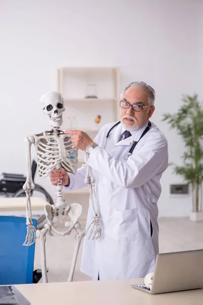 Oude mannelijke dokter die menselijk skelet demonstreert — Stockfoto