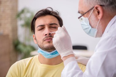 Genç erkek hasta yaşlı doktor otorhinolaryngologis 'i ziyaret ediyor.