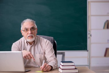 Tahtanın önünde yaşlı bir erkek öğretmen.