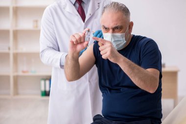 Yaşlı bir erkek hasta aşıyla genç bir doktoru ziyaret ediyor.