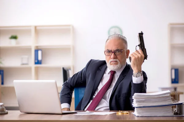 Vieil homme d'affaires tenant une arme sur le lieu de travail — Photo