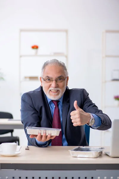 Gammal manlig anställd som äter frukost på kontoret — Stockfoto