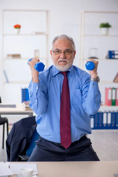 Oude mannelijke werknemer doet sport oefeningen tijdens de pauze — Stockfoto