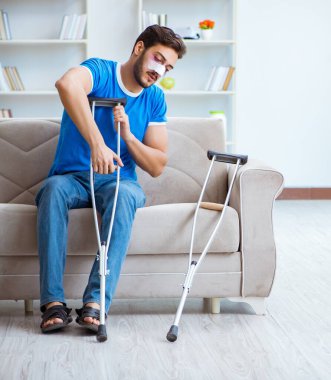 Koltuk değnekli yaralı bir adam evde iyileşiyor.