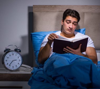 Genç adam yatakta kitap okuyor.