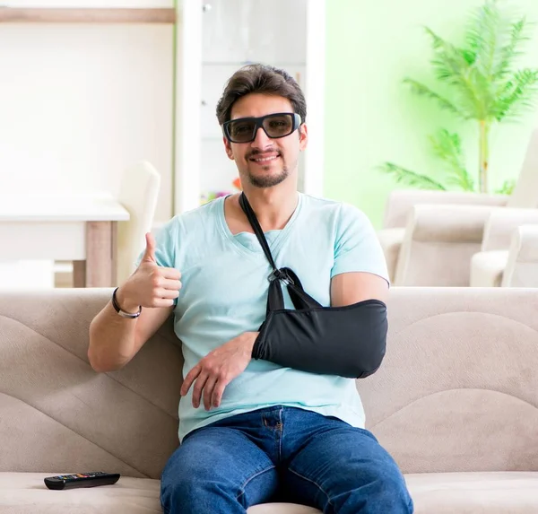 Braço ferido homem sentado no sofá assistindo tv — Fotografia de Stock