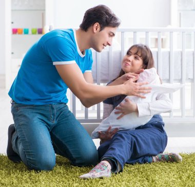 Yeni doğmuş bebekleriyle halıda oturan genç ebeveynler.