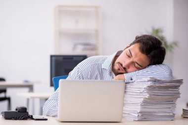 Genç bir erkek çalışan ve ofiste çok fazla iş var.