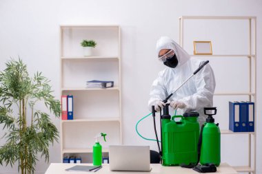 Young male contractor disinfecting office during pandemic