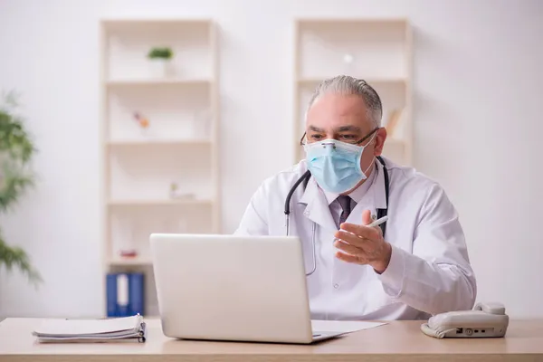 Yaşlı erkek doktor salgın sırasında klinikte çalışıyor. — Stok fotoğraf