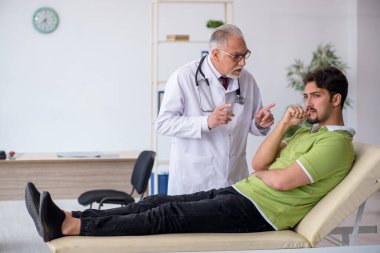 Genç erkek hasta yaşlı erkek doktoru ziyaret ediyor.