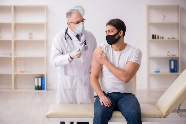 Jonge mannelijke patiënt op bezoek bij oude arts in vaccinatieconcept — Stockfoto
