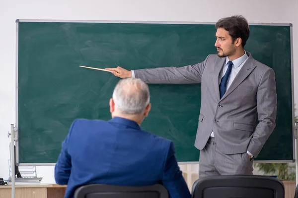 Junge männliche Angestellte und alte Chefin vor der Tafel — Stockfoto