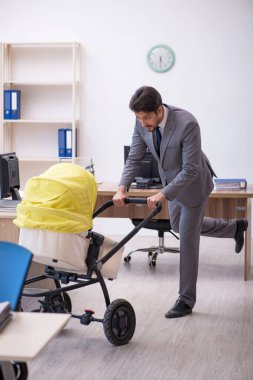 Genç erkek çalışan işyerinde yeni doğan çocuğa bakıyor.