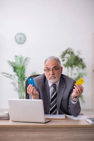 Старий працівник тримає кредитну картку в офісі — стокове фото