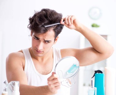 Genç yakışıklı adam aynaya bakıyor.