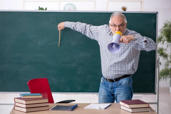 Old male teacher holding megaphone in the classroom — Stock Photo, Image