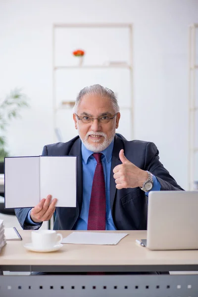 Old male employee reading book in the office — Stock Photo, Image