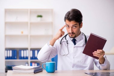 Klinikte kitap okuyan genç bir erkek doktor.