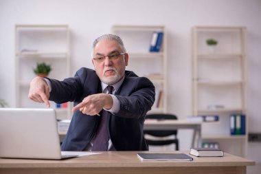 Eski erkek çalışan işyerinde oturuyor.