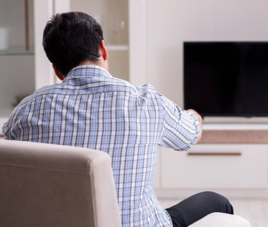 Genç adam evde televizyon izliyor.