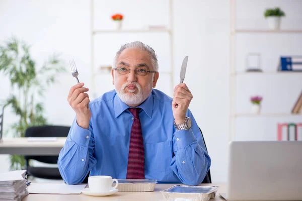 Старый работник-мужчина завтракает в офисе — стоковое фото