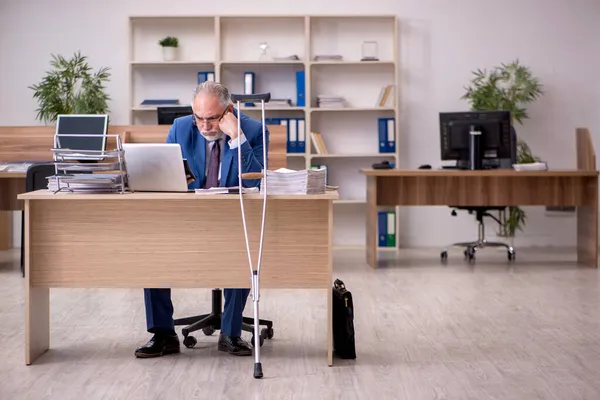 Старый бизнесмен после несчастного случая работает в офисе — стоковое фото