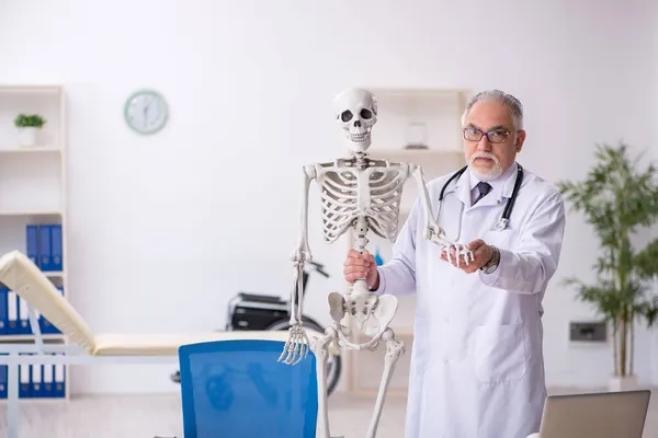 Oude mannelijke dokter die menselijk skelet demonstreert — Stockfoto