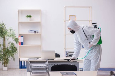 Young male contractor disinfecting office during pandemic