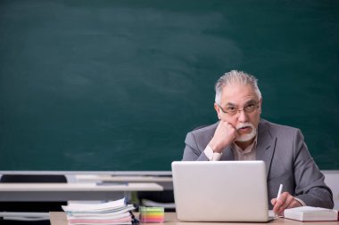 Tahtanın önünde yaşlı bir erkek öğretmen.