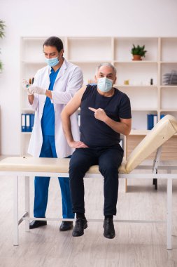 Yaşlı adam covid-19 aşı konseptinde genç doktoru ziyaret ediyor.