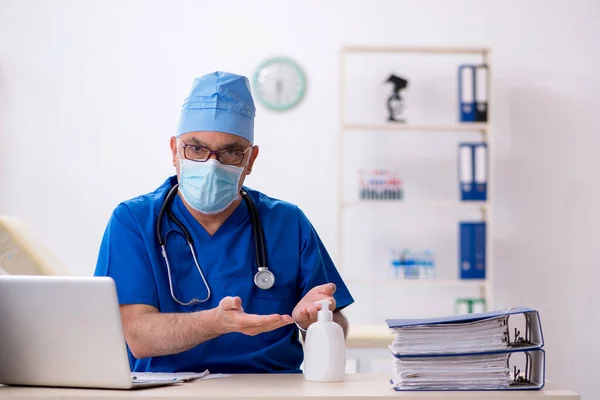 Yaşlı erkek doktor salgın sırasında klinikte çalışıyor. — Stok fotoğraf