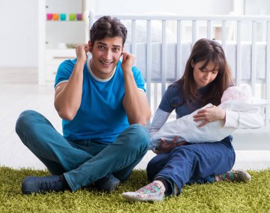 Yeni doğmuş bebekleriyle halıda oturan genç ebeveynler.