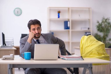 Genç erkek çalışan işyerinde yeni doğan çocuğa bakıyor.