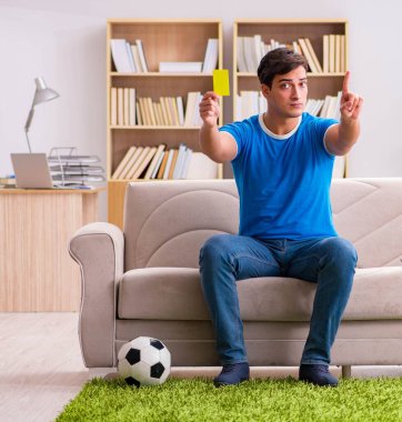 Evdeki kanepede oturup futbol izleyen bir adam.