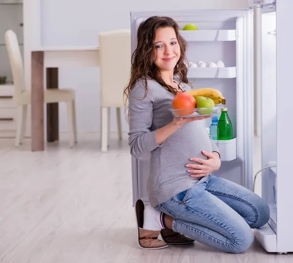 Mulher grávida perto de geladeira à procura de alimentos e lanches — Fotografia de Stock
