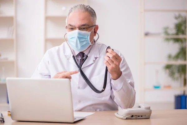 Yaşlı erkek doktor salgın sırasında klinikte çalışıyor. — Stok fotoğraf