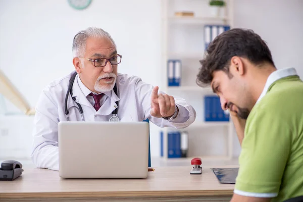 Jonge mannelijke patiënt bezoekt oude mannelijke arts — Stockfoto