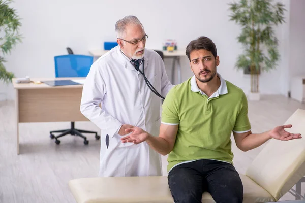 Young man visiting old male doctor — Stock Photo, Image