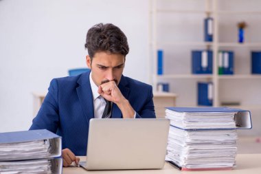 Genç bir erkek çalışan ve ofiste çok fazla iş var.