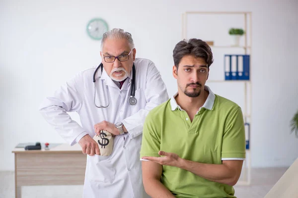 Genç erkek hasta pahalı ilaçlarla yaşlı erkek doktoru ziyaret ediyor. — Stok fotoğraf
