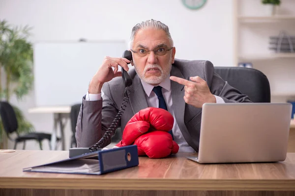 Velho empresário empregado usando luvas de boxe no local de trabalho — Fotografia de Stock