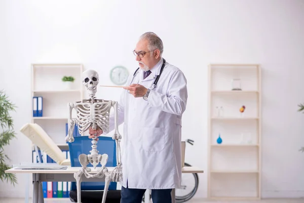 Oude mannelijke dokter die menselijk skelet demonstreert — Stockfoto