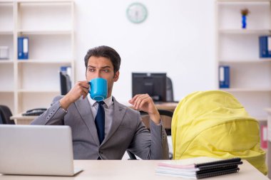 Genç erkek çalışan işyerinde yeni doğan çocuğa bakıyor.