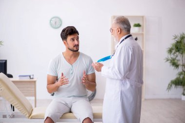 Genç erkek hasta yaşlı erkek doktoru ziyaret ediyor.